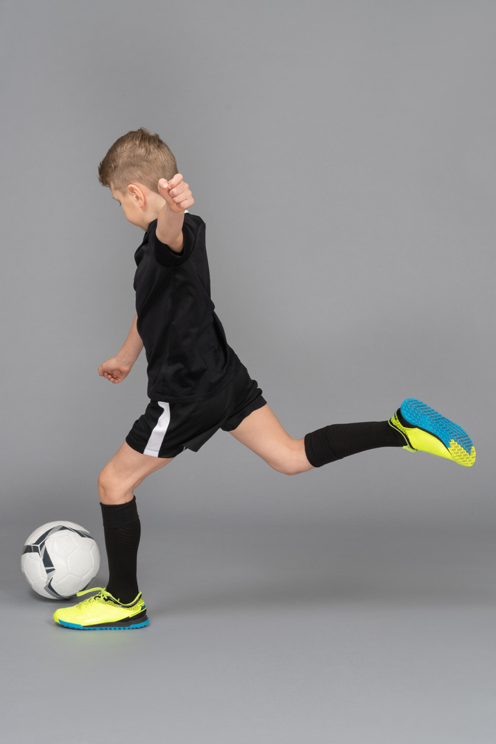Side view of a kid boy in football uniform kicking a ball