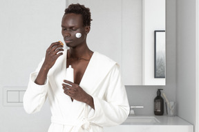 A man in a bathrobe putting on face cream