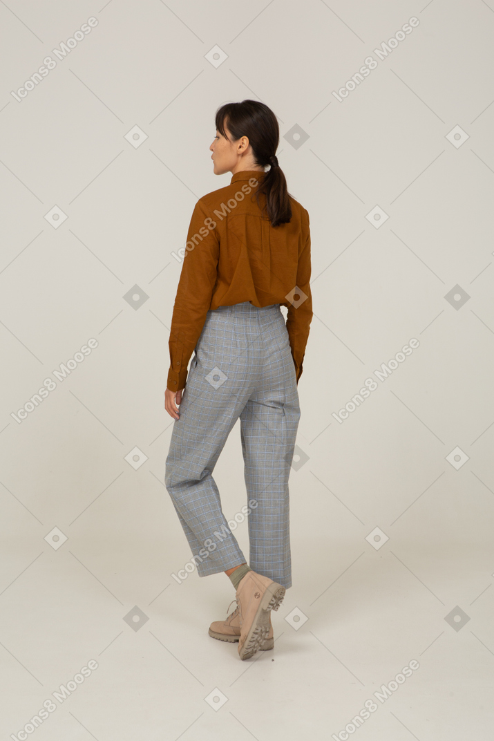 Vista posterior de tres cuartos de una joven mujer asiática haciendo pucheros en calzones y blusa