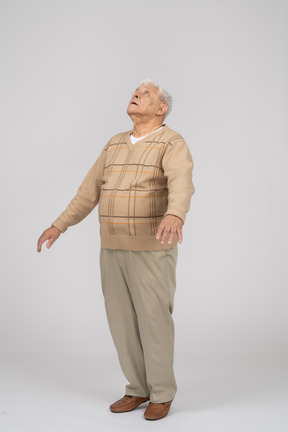 Front view of an impressed old man standing on toes and looking up