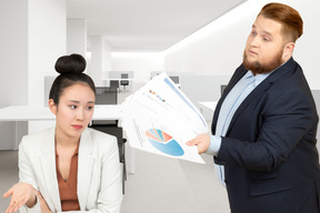 A man in a suit showing papers with graphs to a woman in the office