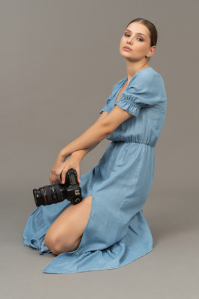 Side view of a young woman in blue dress sitting on a floor with camera