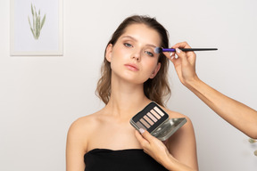 Vista frontal de una maquilladora haciendo maquillaje de ojos para una modelo femenina