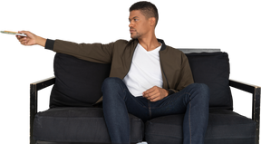 Front view of young man sitting on a sofa and passing pensil with notebook