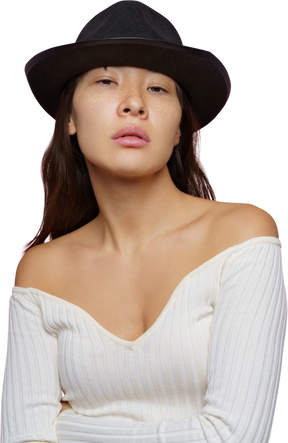 Vista frontal de uma jovem mulher de chapéu preto, olhando para a câmera de forma crítica