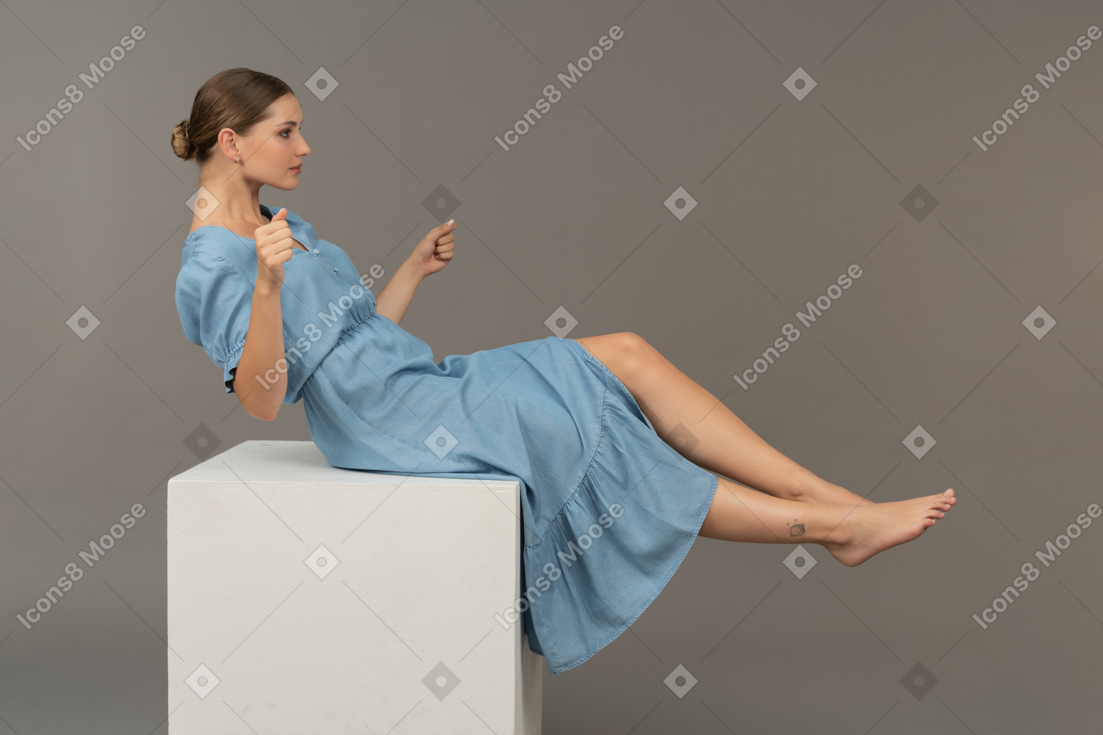 年轻女子坐在立方体上试图保持平衡的侧视图