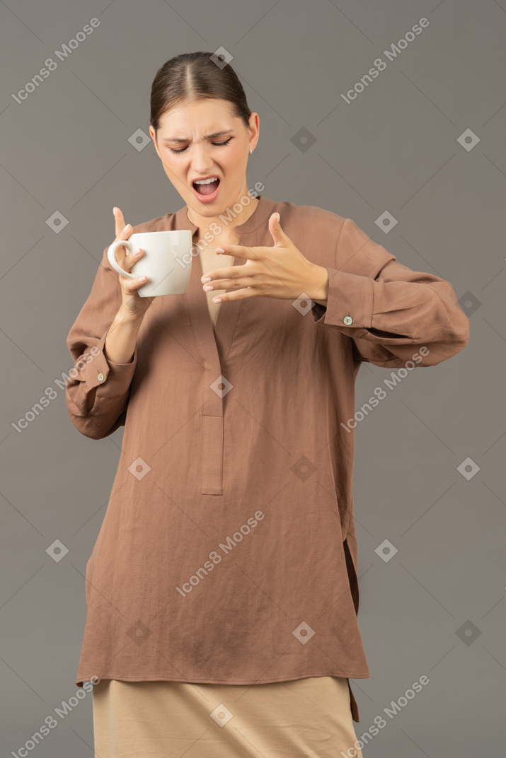 Mujer joven se quema la yema del dedo con café caliente