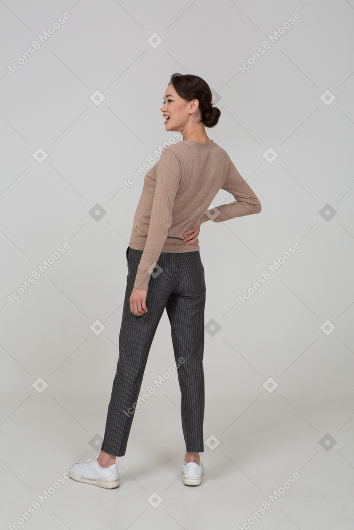 Three-quarter back view of a laughing female in pullover and pants putting hand on hip