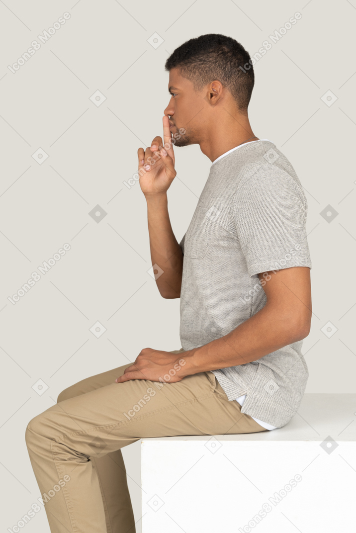A good looking young guy sitting on the white chair and holding his finger close to his mouth
