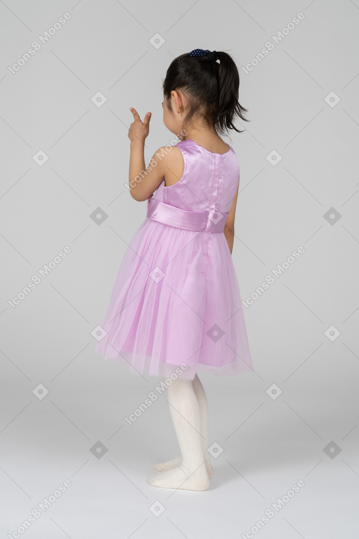 Mädchen im rosafarbenen kleid, das mit einer fingerpistole zielt