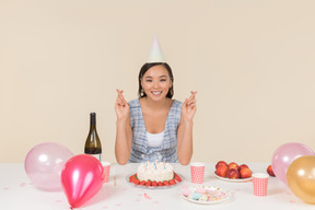 Jovem menina asiática sentado à mesa de aniversário e assobiando