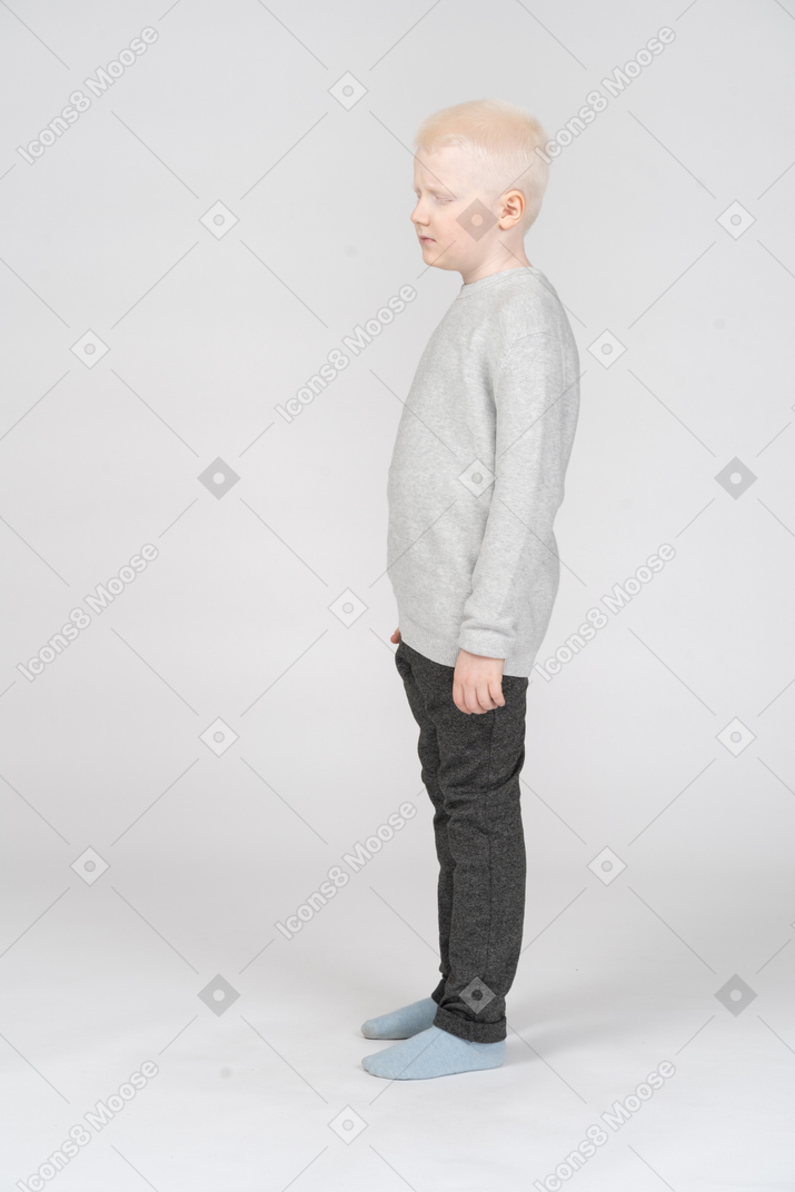 A miserable blonde little boy standing with his eyes closed