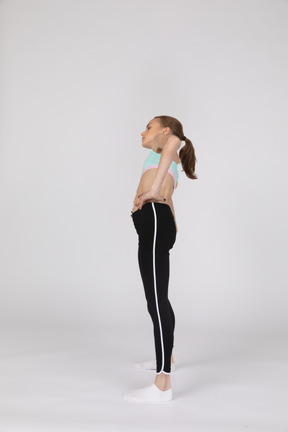 一个十几岁的女孩在运动服蹲着，把手放在臀部上的侧视图