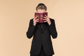 Young man in a black suit and a kippah praying with a torah in his hands