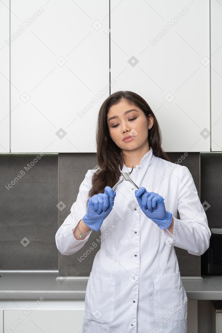 Front view of a young female doctor in protective gloves looking at her dental equipment