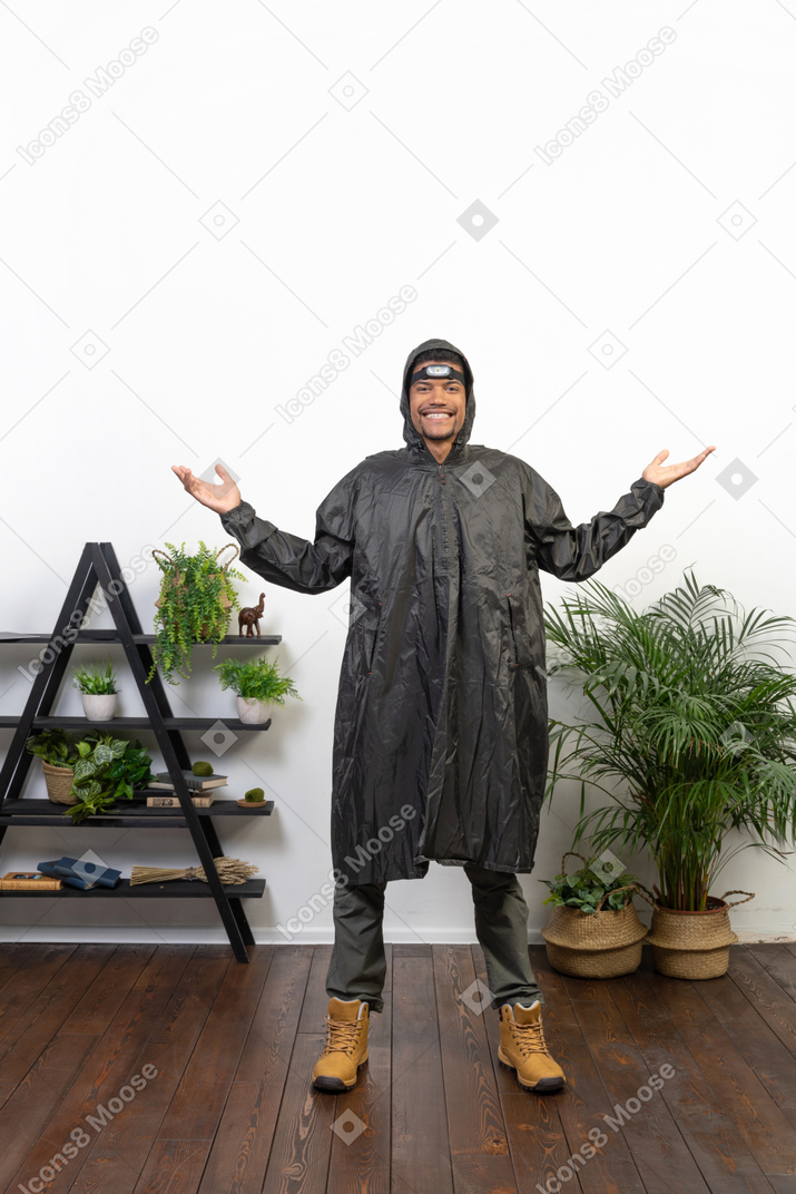 Homem sorridente com capa de chuva, encolhendo os ombros e abrindo os braços