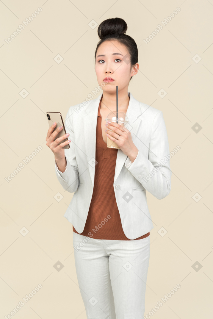 Pensive young asian office employee holding phone and having coffee