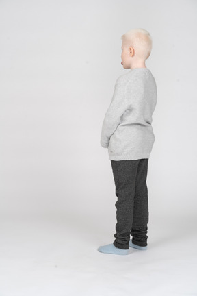 Vista traseira de três quartos de um garoto com roupas casuais, mostrando a língua