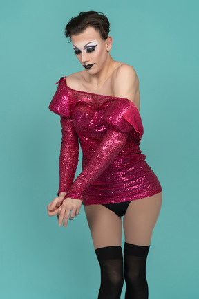 Drag queen en maquillaje de escenario quitándose el vestido rosa