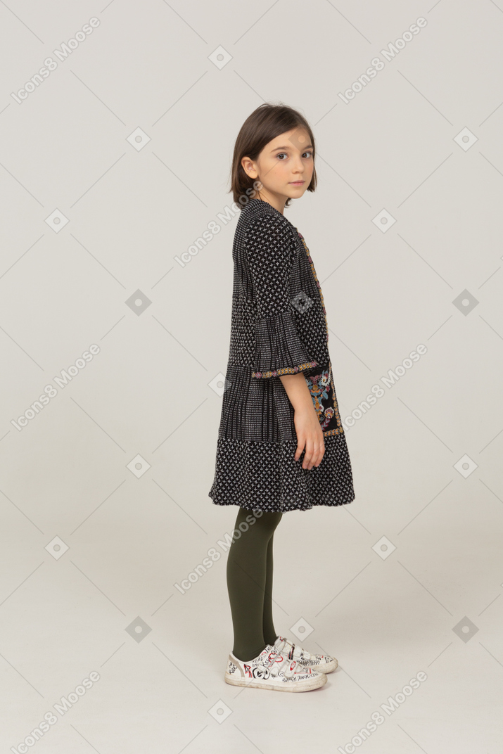 Side view of a little girl in dress turning head and looking at camera