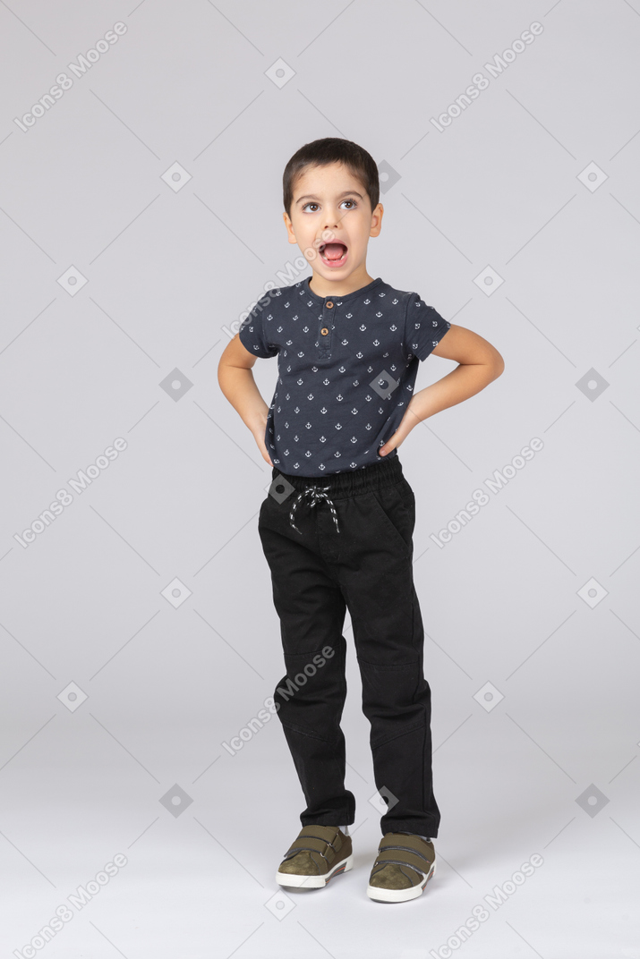 Front view of an emotional cute boy posing with hands on hips