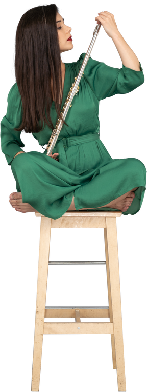 Figura intera di una giovane donna che guarda il clarinetto seduto con le gambe incrociate su una sedia di legno