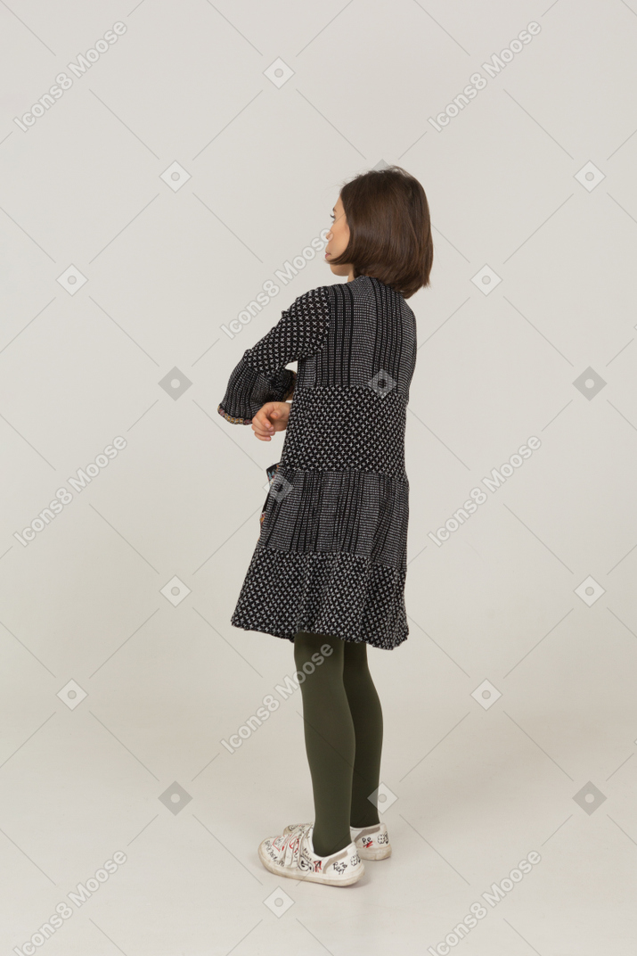 Vista posteriore di tre quarti di una bambina vestita che incrocia le braccia