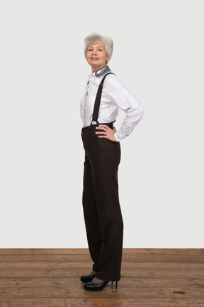 Side view of a proud old lady putting hands on hips in office clothing