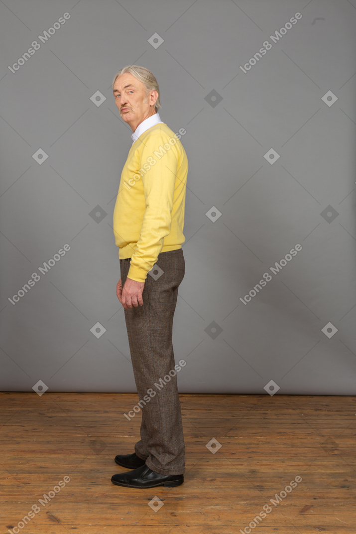 Вид сбоку надутого старика в желтом пуловере, смотрящего в камеру