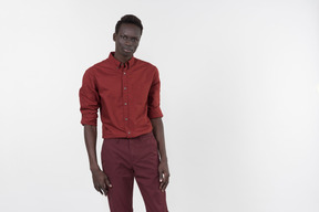 A young black man in a red shirt with rolled up sleeves and dark red pants standing alone on the white background