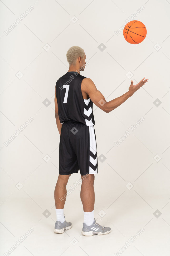 Vista posterior de tres cuartos de un joven jugador de baloncesto masculino lanzando una pelota