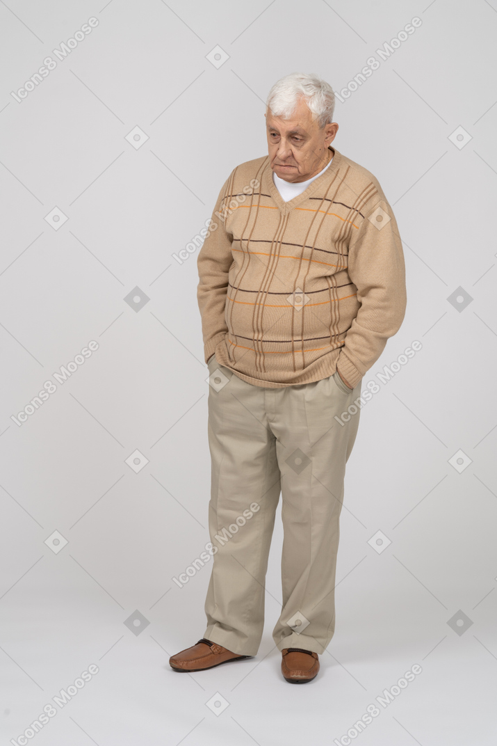 一个穿着休闲服、双手插在口袋里站着的悲伤老人的正面图