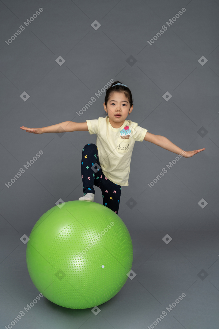 Kleines mädchen, das mit ausgebreiteten armen auf einen grünen fitball tritt