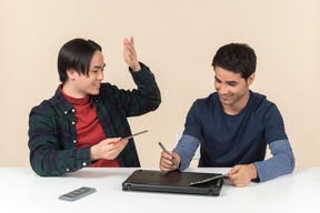 Deux jeunes geeks souriants assis à la table et fixant un ordinateur portable