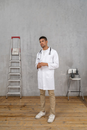 Vista de tres cuartos de un joven médico de pie en una habitación con escalera y silla tomados de la mano juntos