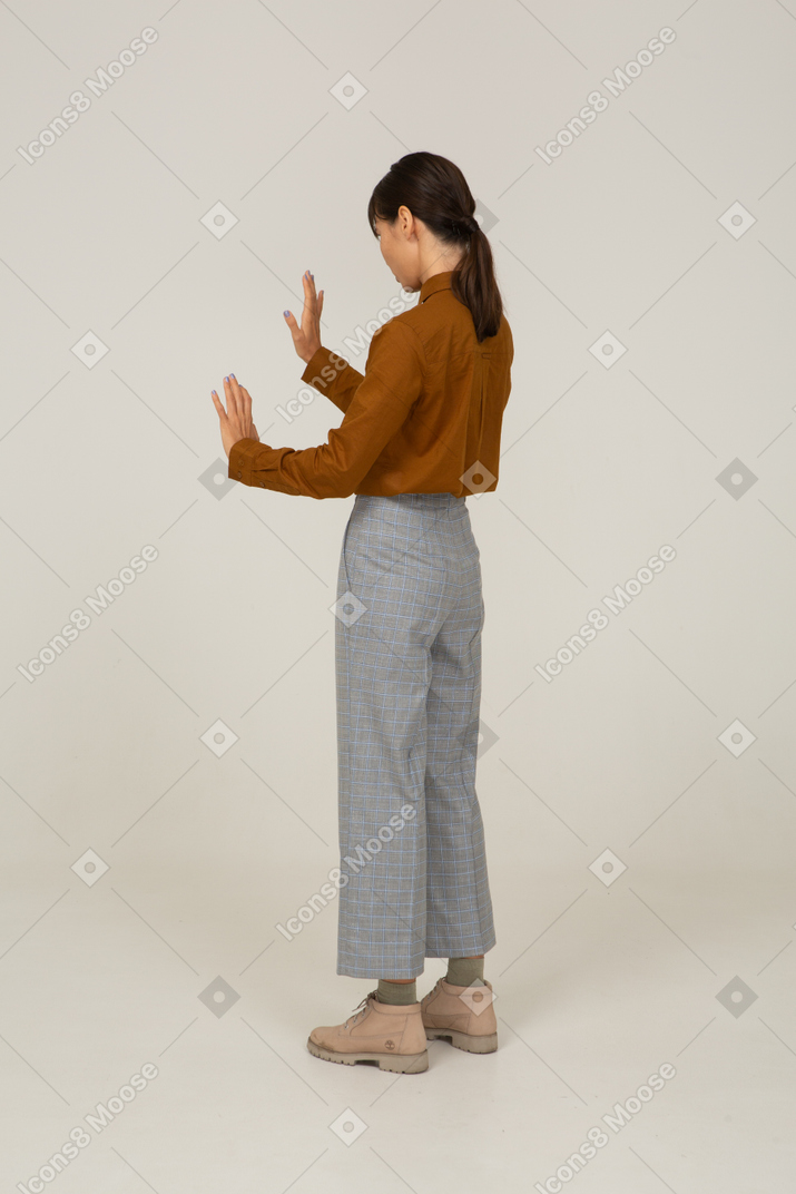 Vista traseira a três quartos de uma jovem mulher asiática de calça e blusa, estendendo os braços