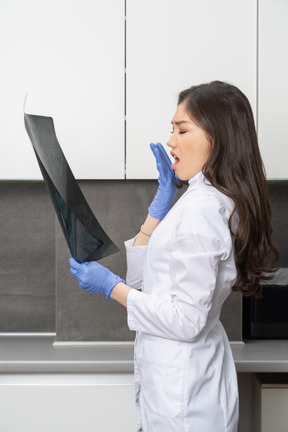 Side view of a shocked female doctor looking at x-ray image and hiding her mouth