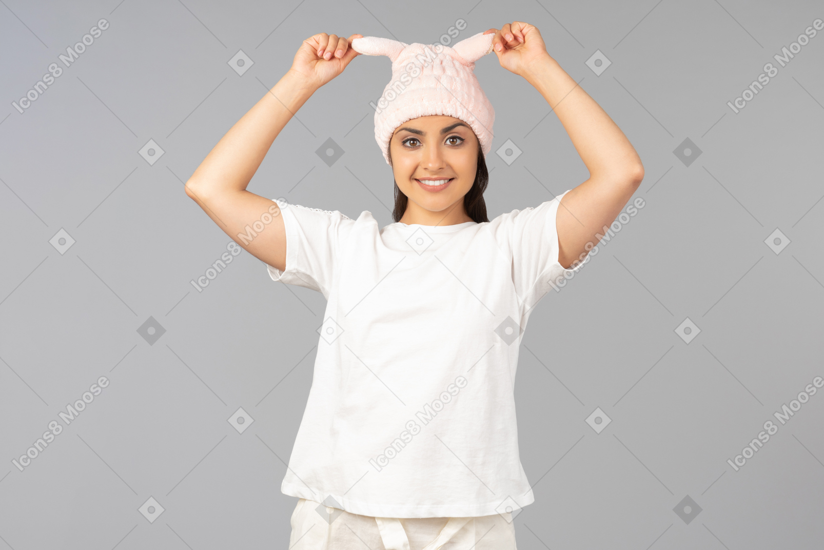 Joven mujer india en ropa de casa tocando conejo rosa como sombrero que lleva puesto