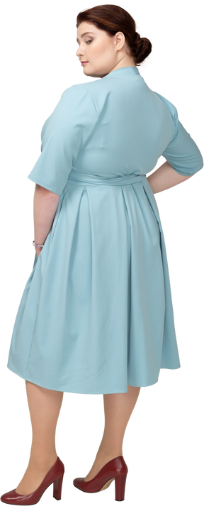 Вид сзади женщины в синем платье позирует с рукой на бедре