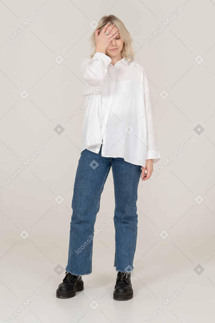 Front view of a blonde female in casual clothes standing still and hiding face