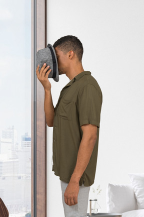 Man standing in a room and covering his face with a hat