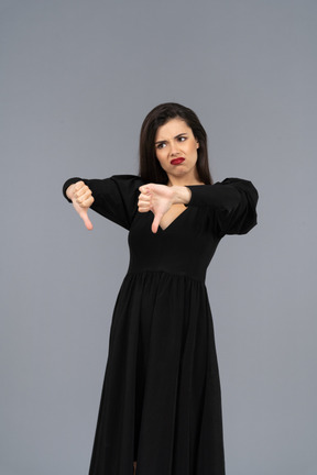 Vue de trois quarts d'une jeune femme mécontente en robe noire mettant les pouces vers le bas