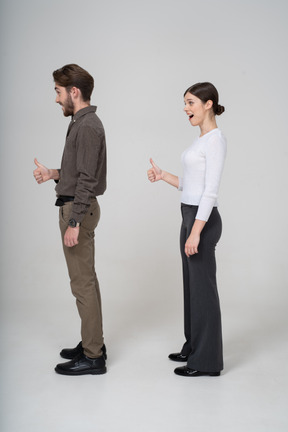 Side view of a cheerful young couple in office clothing showing thumb up