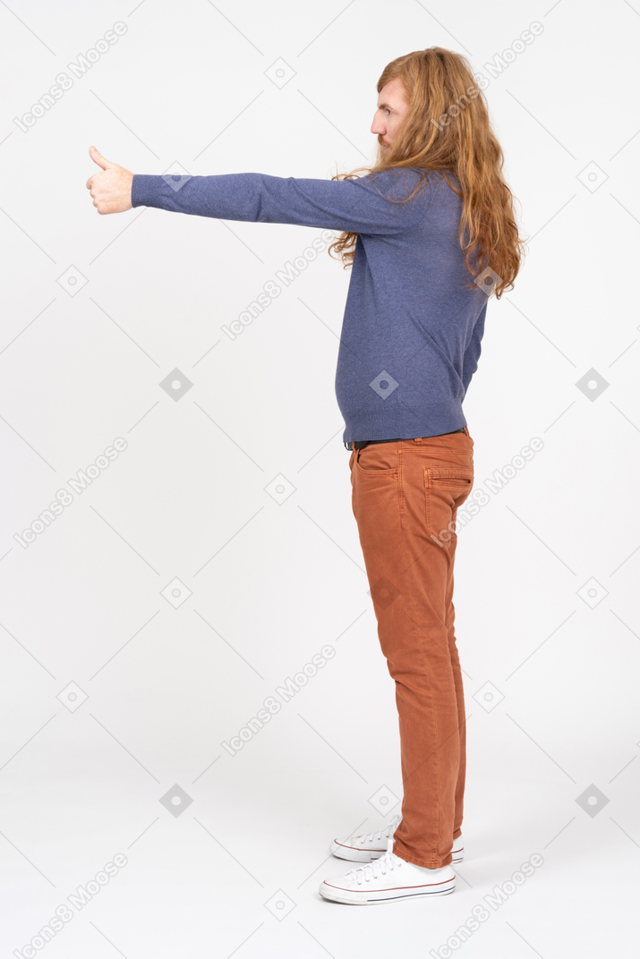 Вид сбоку на молодого человека в повседневной одежде, показывающего большой палец вверх