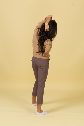 Three-quarter back view of a dark-skinned young female touching hair