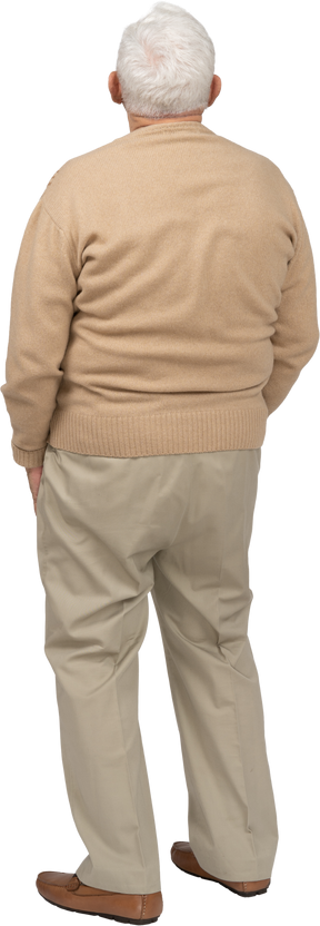 Vista trasera de un anciano con ropa informal de pie con las manos en los bolsillos y mirando hacia arriba
