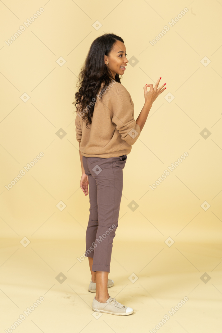 Vista lateral de uma jovem mulher de pele escura mostrando um gesto de ok