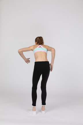 Back view of a teen girl in sportswear leaning forward while standing like a robot
