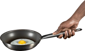 Human arm holding a fried egg on pan
