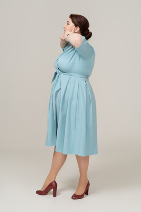 Side view of a woman in blue dress touching her mouth